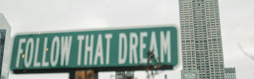 Schild ' Follow that dream' vor Hochhaus