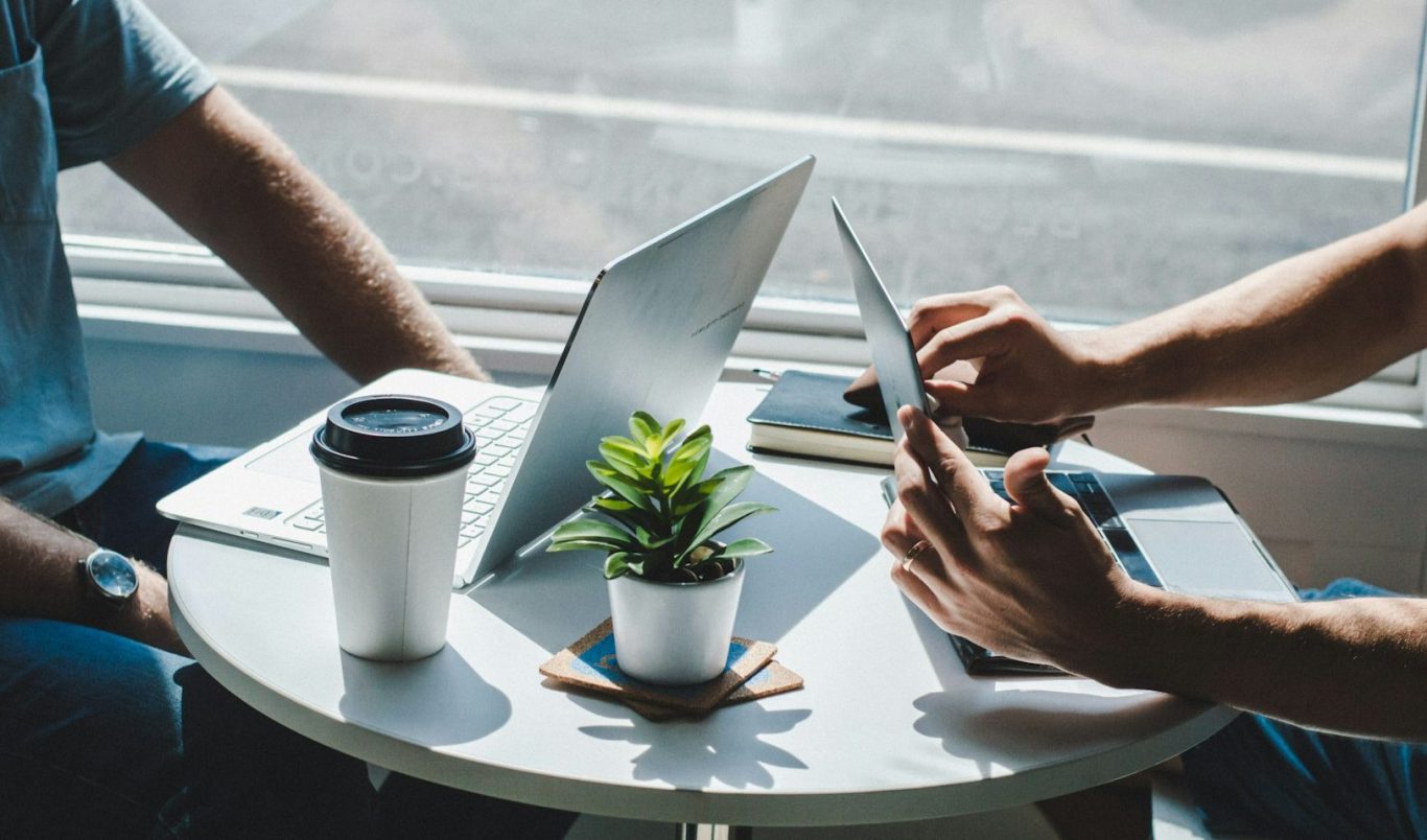 Zwei Personen sitzen an einem Tisch mit Laptops Zwei Personen sitzen an einem Tisch mit Laptops und Kaffee, eine kleine Pflanze in der Mitte.